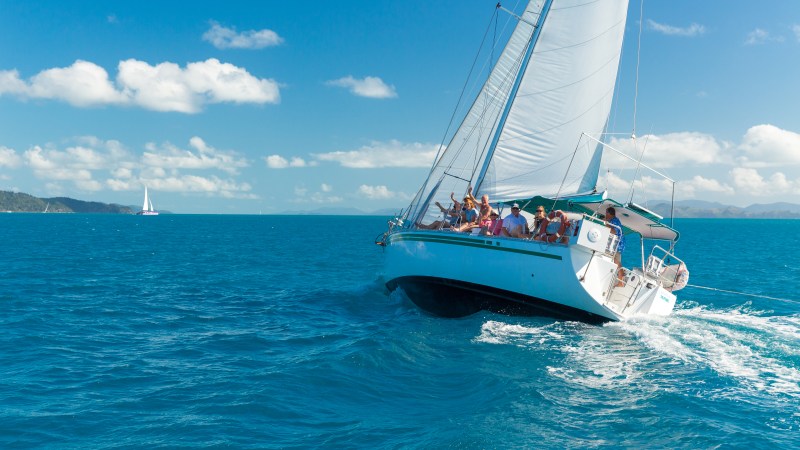 Sailboat with people sailing on a clear blue ocean under a sunny sky.