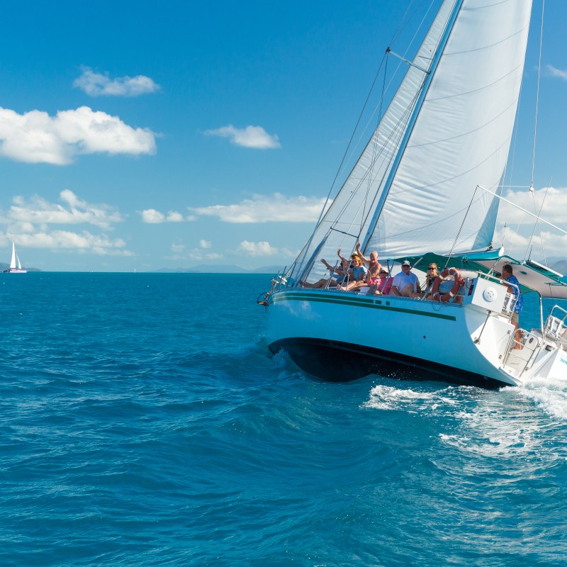 Sailboat with people sailing on a clear blue ocean under a sunny sky.