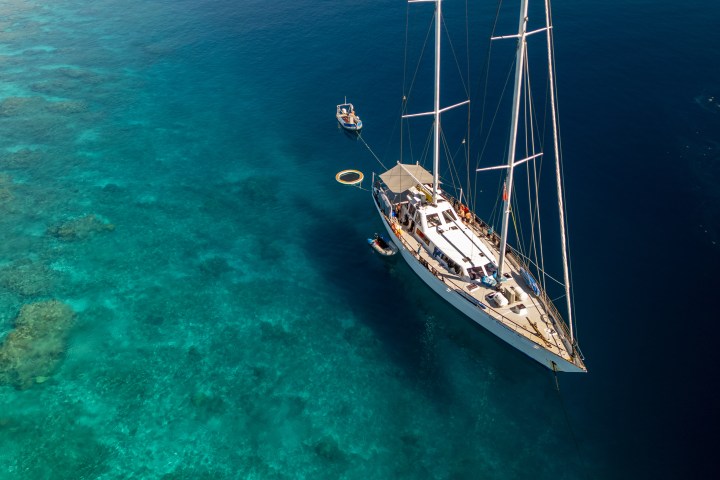 Sailboat on clear blue water with visible coral reefs below.