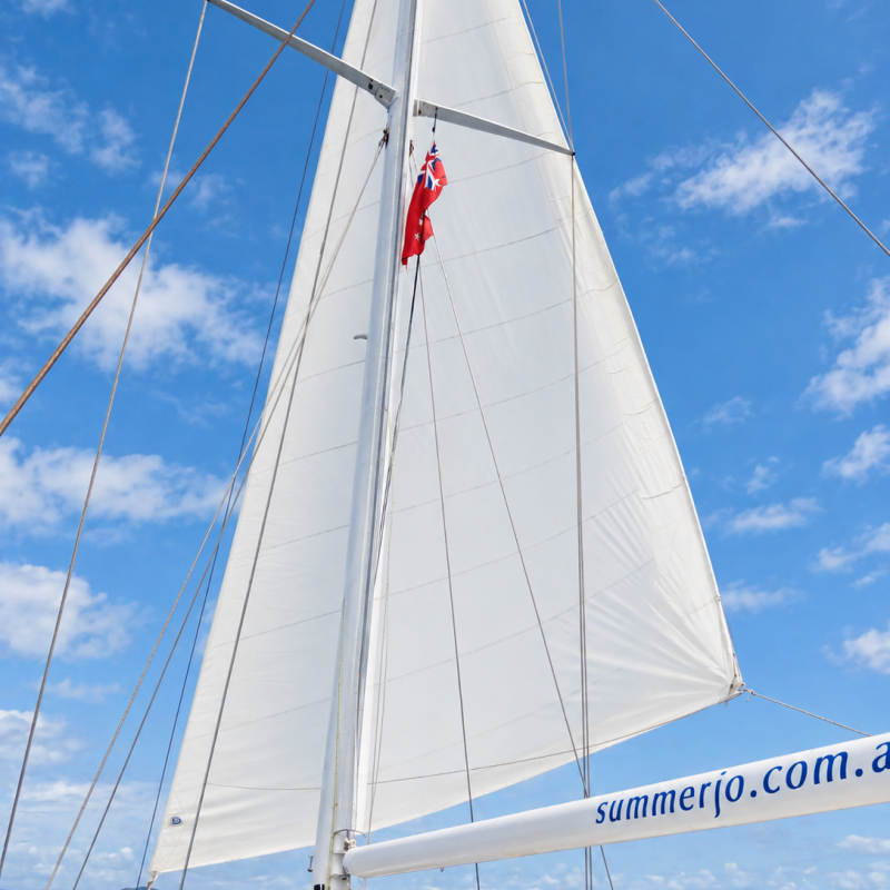 Sailboat mast with white sail against a blue sky.