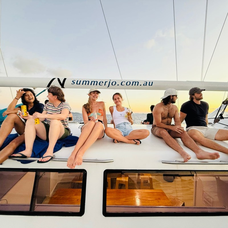 Group of young adults sitting on a sailboat deck at sunset.