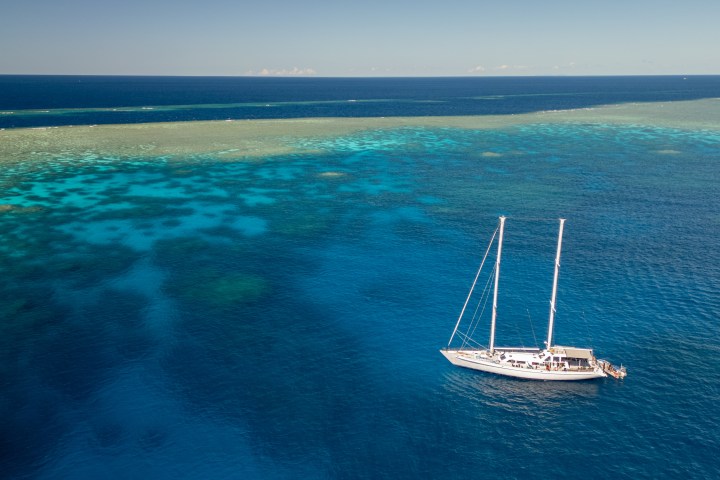 Sailboat on clear blue ocean, near coral reef, under clear sky.