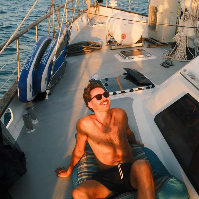 Man relaxing on a boat deck at sea during sunset.