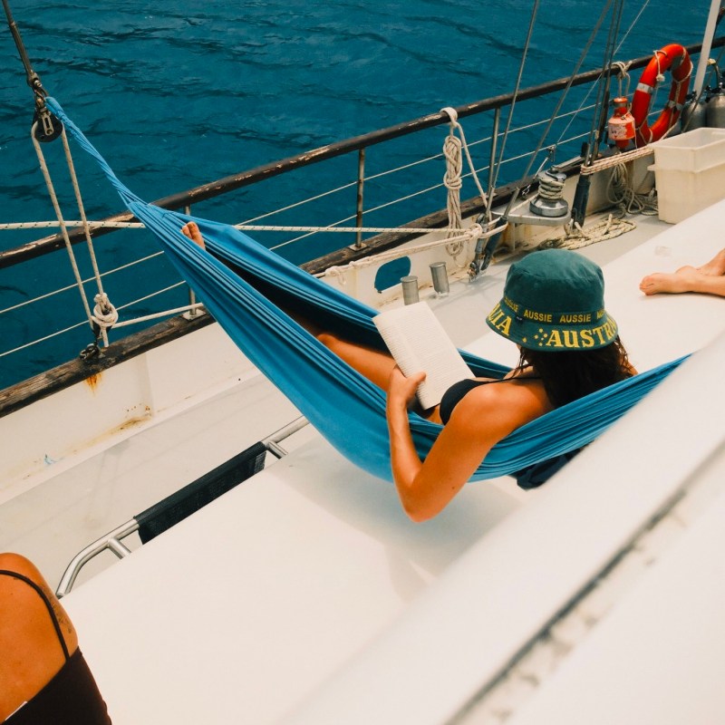 Person reading in a hammock on a boat with a blue ocean view.