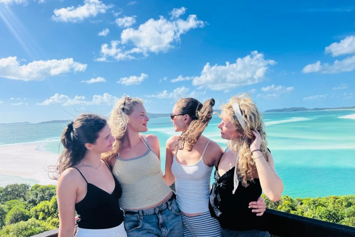 Four people smiling at a beach viewpoint with turquoise water.