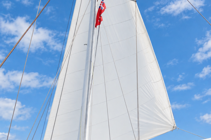 Sailboat mast with white sails against a clear blue sky.