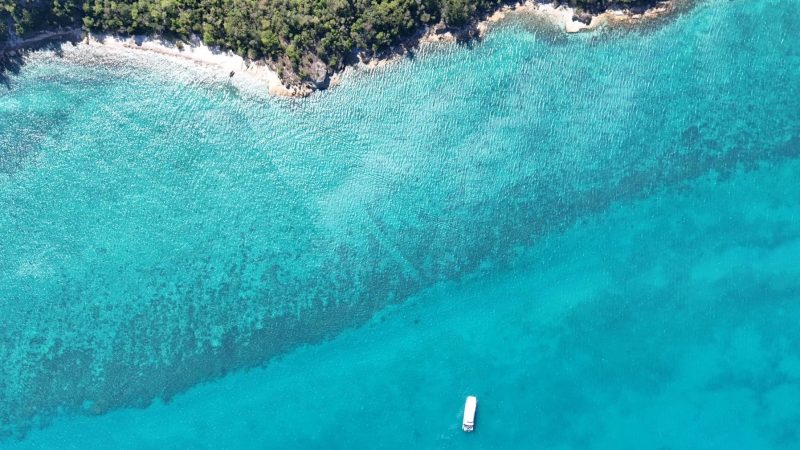 Aerial view of turquoise sea with several small boats and a rocky coastline.