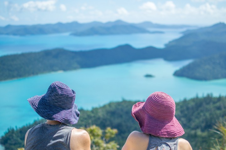 Two people in hats overlooking a scenic view of blue waters and distant islands.
