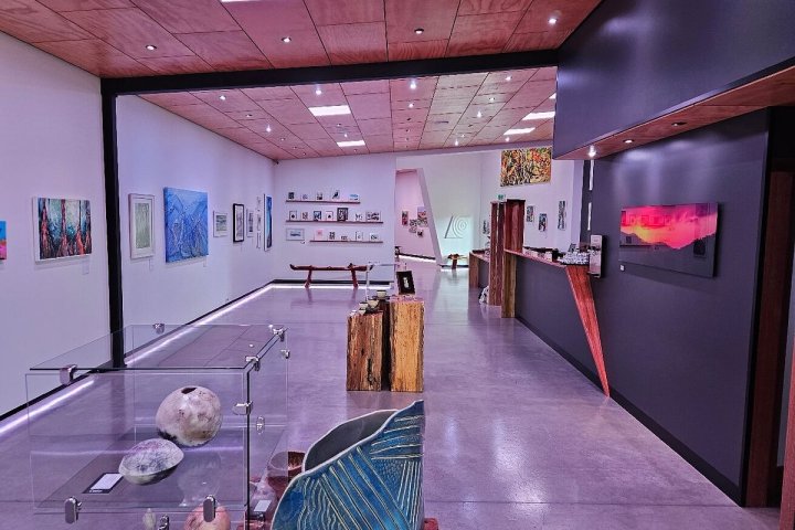 Art gallery interior with paintings on walls, wooden sculpture, and glass display case with shells.