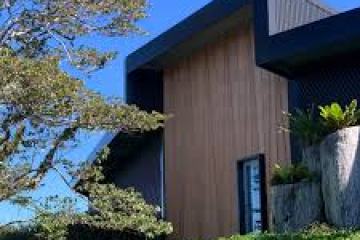 Modern house with wooden facade, large tree, and clear blue sky.