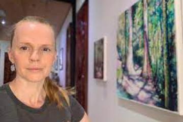 Person standing indoors near wall with forest painting.