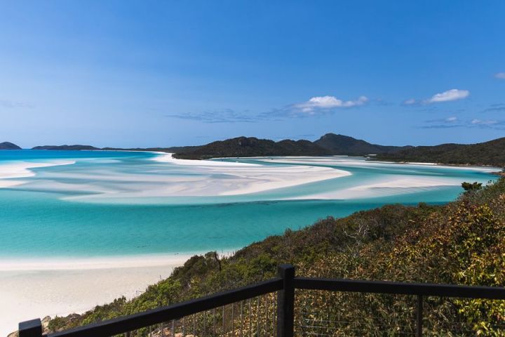 Scenic view of turquoise sea, sandy beach, and distant mountains under a clear blue sky.