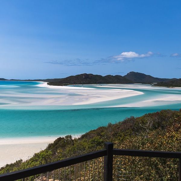 Scenic view of turquoise sea, sandy beach, and distant mountains under a clear blue sky.