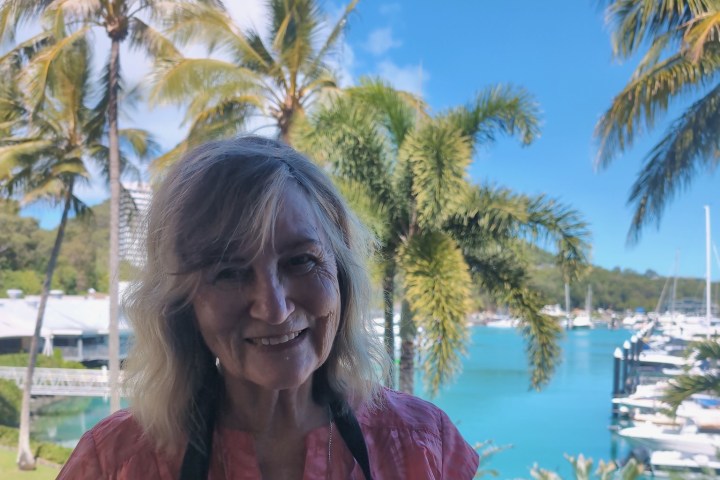 Smiling woman in front of palm trees and marina on a sunny day.