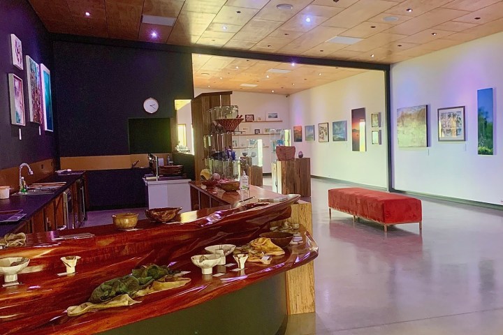 Art gallery interior with wooden counter, red bench, and framed artworks on walls.