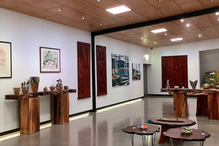 Art gallery with wood sculptures, pottery, and paintings on display in a modern setting.