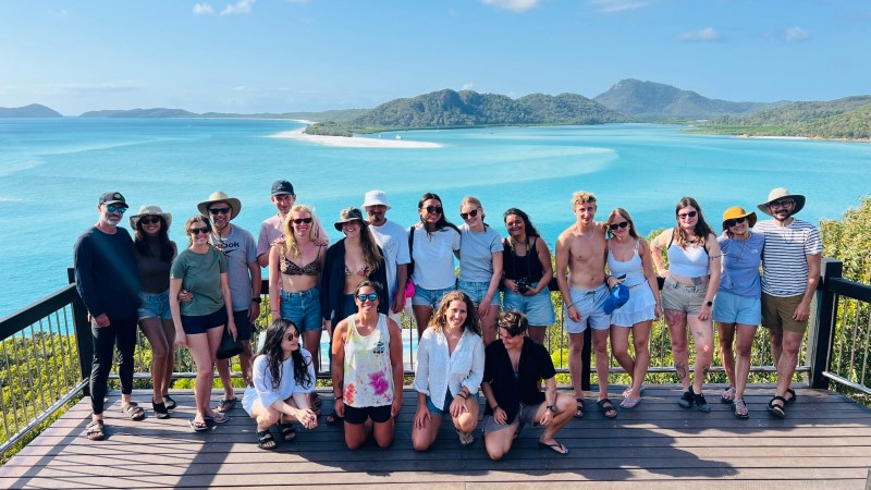 Group of people posing on a deck with an ocean view in the background.
