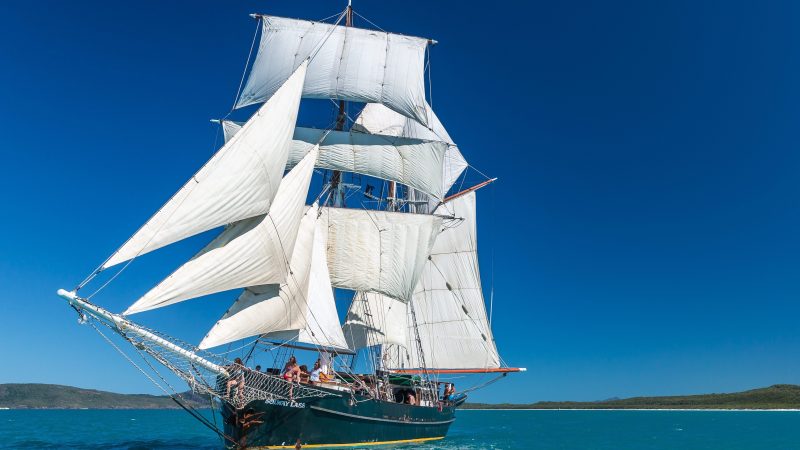 Sailing ship with white sails on turquoise sea under clear blue sky.