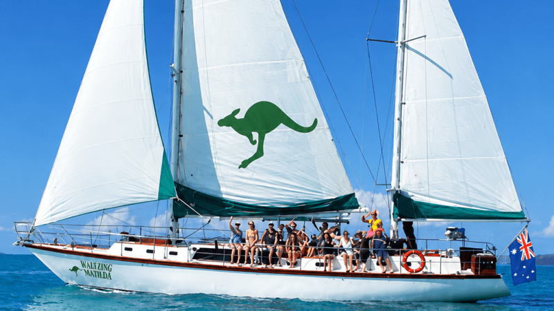 Sailboat with kangaroo print and group of people, sailing on clear blue water.